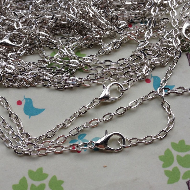 May include: A silver chain with two lobster clasps. The chain is made of small, oval-shaped links.