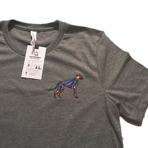 Könnte beinhalten: Ein heidefarbenes T-Shirt mit einem bunten geometrischen Design eines Hundes auf der linken Brust. Das Etikett auf dem Shirt lautet "Wetherby" und hat die Größe "5" und das Datum "22" aufgedruckt.