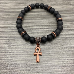 May include: Black beaded bracelet with a copper Ankh pendant. The beads have a matte finish and copper accents.