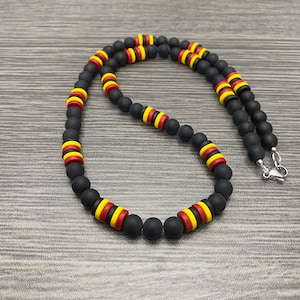 May include: A black beaded necklace with yellow and red stripes on each bead. The necklace is made of matte black beads and has a silver clasp.
