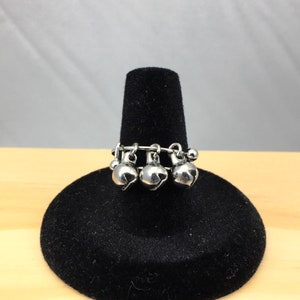 May include: A silver ring with four small bells hanging from it. The ring is on a black velvet display stand.