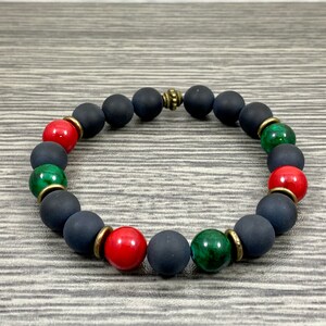 May include: A black beaded bracelet with red and green gemstone beads and gold accents.
