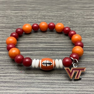May include: A maroon and orange beaded bracelet with a football charm and a VT charm.
