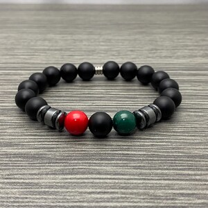 May include: Black beaded bracelet with red and green accent beads. The bracelet features matte black beads, interspersed with metallic gray spacers and a red and green bead. A stylish accessory.