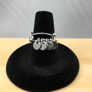 May include: A silver ring with a series of small, round, silver charms hanging from a silver band.