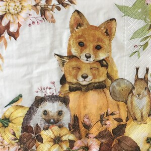 Pode incluir: Guardanapo de papel decorativo com cena de outono. Apresenta duas raposas, um ouriço, um esquilo e um pássaro, rodeados por abóboras, flores e folhagens em tons quentes. O design é temático de outono.