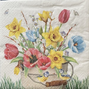 May include: A decorative paper napkin featuring a watercolor illustration of a floral bouquet. The bouquet includes yellow daffodils, red and pink tulips, and blue flowers in a metal bucket. Two small birds perch on the bucket's handle, with butterflies fluttering above.