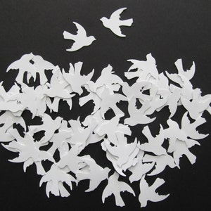 Puede incluir: Una gran cantidad de recortes de papel blanco en forma de pájaros. Los pájaros están todos mirando en la misma dirección y están dispuestos en un grupo suelto.