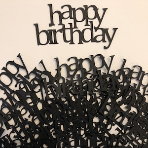 Può includere: Confeti di carta nera con le parole "happy birthday" in un carattere grande. I confetti sono sparsi su una superficie bianca. Ci sono anche due pezzi di confetti più grandi con le parole "happy birthday" in un carattere più grande.