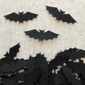 May include: A pile of black paper bats, with three larger bats scattered on a white background.