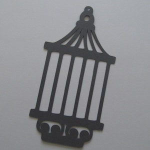 以下が含まれることがあります： 装飾的なトップが付いた鳥かごの黒い紙切り抜き。ケージは、縦のバーと丸みを帯びたベースを持つシンプルなデザインです。