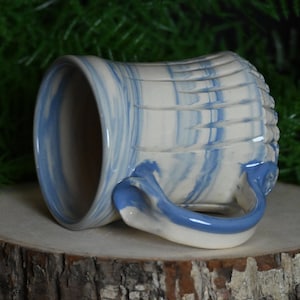 May include: A handmade ceramic mug with a blue and white marbled glaze. The mug has a unique, textured design and a curved handle.