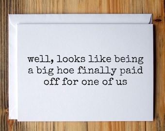 Puede incluir: Una tarjeta de felicitación blanca con un sobre a juego, con el texto en negro: "well, looks like being a big hoe finally paid off for one of us". Sobre un fondo de madera.