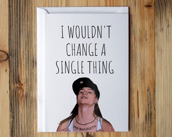 May include: A white card with the text "I wouldn't change a single thing" and a cartoon image of a person with long hair and a black hat. The person has a tattoo that says "No Regrets".
