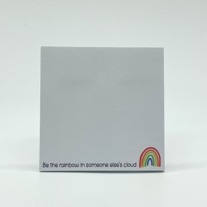 May include: White notepad with the text "Be the rainbow in someone else's cloud" and a rainbow graphic.
