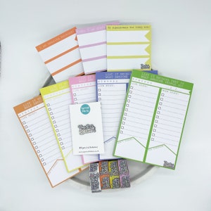May include: A set of colorful to-do list notepads with different motivational phrases. The notepads are on a white plate with washi tape. The notepads have a checklist and space to write. One notepad says "List it because that is what awesome people do!" Another notepad says "List it because what awesome people do!"
