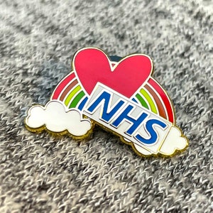 May include: A vibrant enamel pin with a red heart, rainbow, and white cloud design. The pin displays the letters "NHS" in blue and white, with a gold border. The pin is set against a grey background.