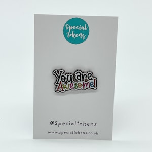 May include: A colorful enamel pin with the text "You are Awesome!" on a white card with the text "Special Tokens" and a website address.