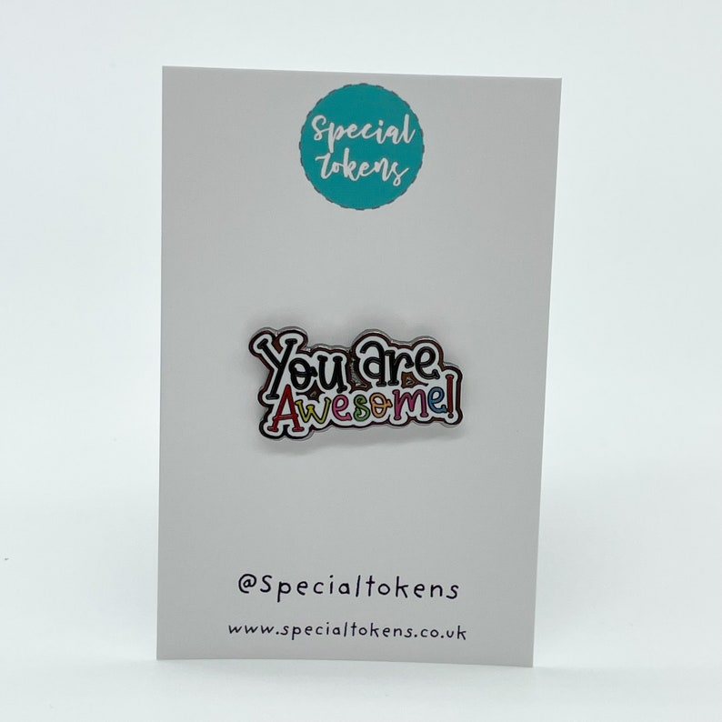 May include: A colorful enamel pin with the text "You are Awesome!" on a white card with the text "Special Tokens" and a website address.