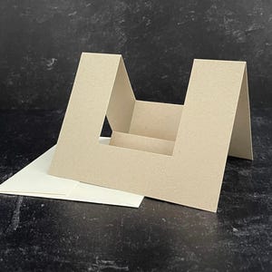 May include: A brown cardstock card with a cut-out window in the shape of a U. The card is folded to create a stand-up display.