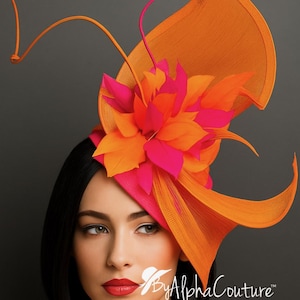 Puede incluir: Un fascinador naranja y rosa vibrante con un diseño floral. El tocado presenta una flor grande y estilizada y acentos curvos y fluidos. El texto "By Alpha Couture" es visible.