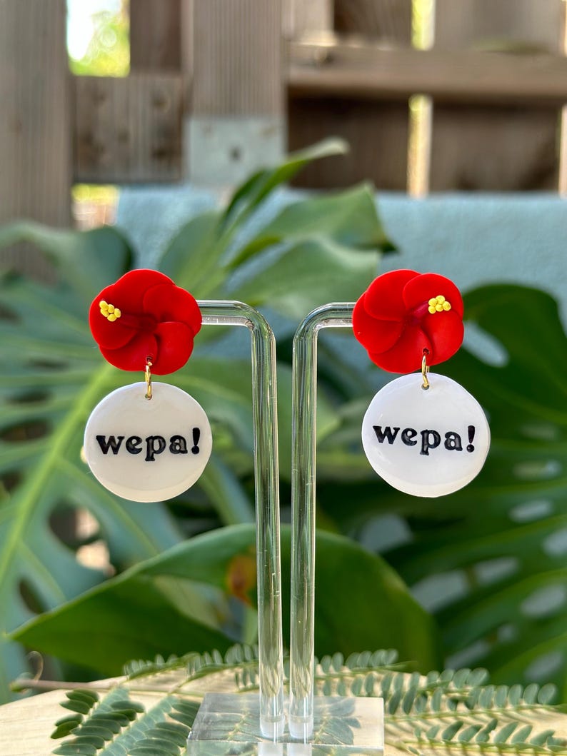 May include: A pair of red flower earrings with white round charms that say "wepa!" in black lettering.