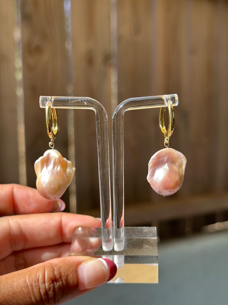 May include: A pair of gold hoop earrings with a large, pink baroque pearl dangling from each hoop.