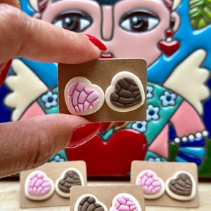 May include: A set of four pairs of heart-shaped earrings. Each pair features a pink and white heart-shaped earring and a brown heart-shaped earring. The earrings are displayed on brown card stock.
