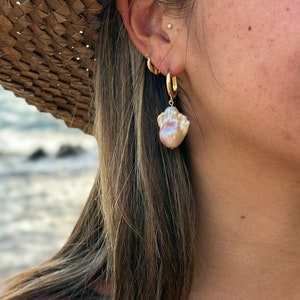 May include: A pair of gold hoop earrings with a large, iridescent pearl dangling from one earring.