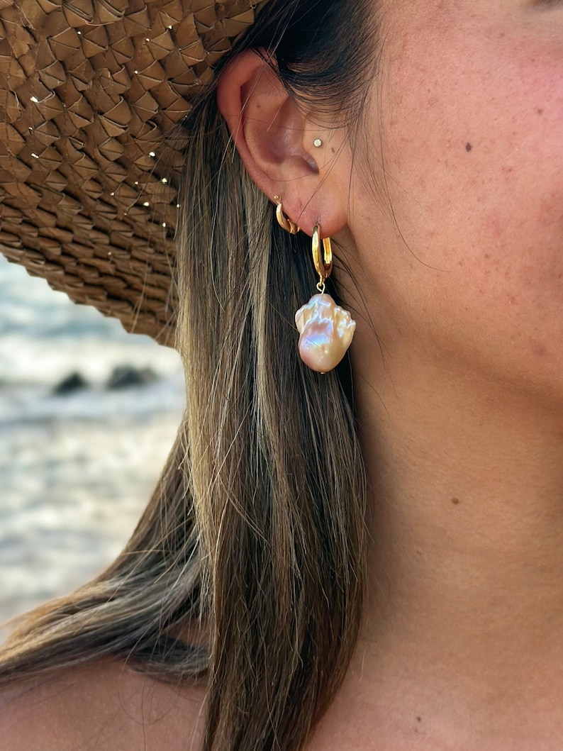 May include: A pair of gold hoop earrings with a large, iridescent pearl dangling from one earring.