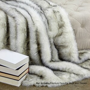 K&ouml;nnte beinhalten: Eine wei&szlig;e und schwarze Kunstfell-Decke mit einem langen, zotteligen Flor. Die Decke ist gefaltet und &uuml;ber ein M&ouml;belst&uuml;ck gelegt. Der Text "Fur Accents&reg; Premium Faux Fur Rugs and Throws" ist in der unteren rechten Ecke des Bildes sichtbar.