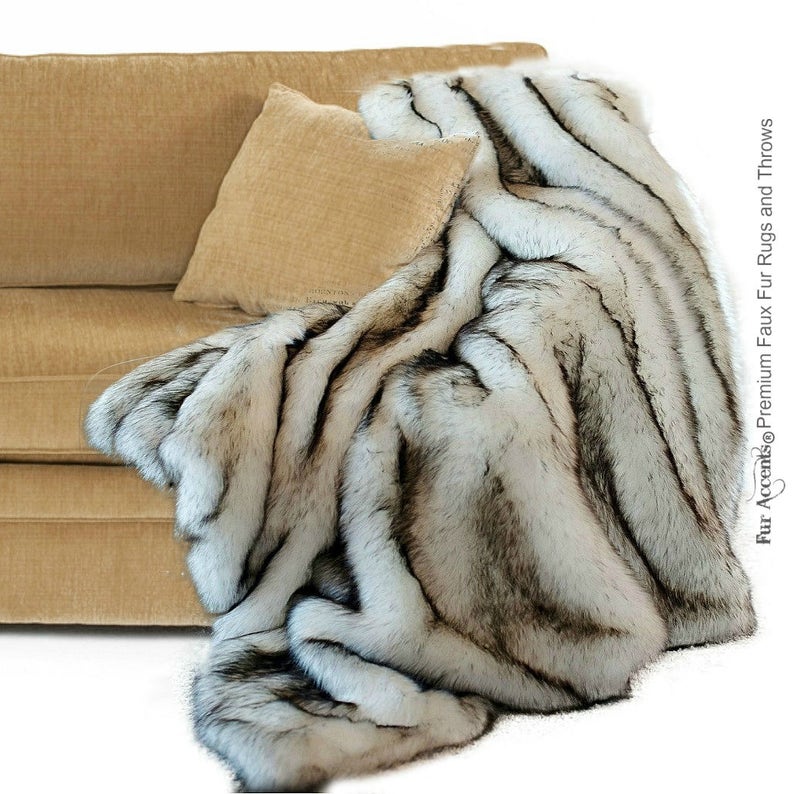 K&ouml;nnte beinhalten: Eine wei&szlig;e und schwarze Kunstfelldecke, die &uuml;ber ein beiges Sofa gelegt ist. Die Decke hat einen langen, zotteligen Flor und ist aus weichem, luxuri&ouml;sem Kunstfell gefertigt.