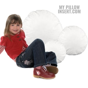 May include: A young person sitting on three large white round pillows. The pillows are all different sizes. The person is wearing blue jeans and red shoes. The text "MY PILLOW INSERT.COM" is in the upper right corner of the image.
