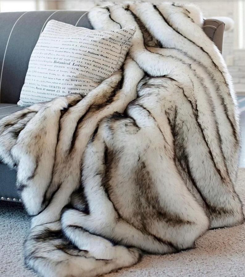 Pu&ograve; includere: Una coperta in pelliccia sintetica bianca e nera con un motivo a righe. La coperta &egrave; drappeggiata su un divano grigio.
