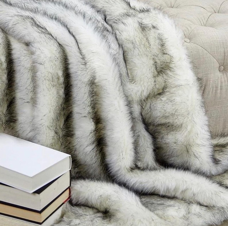 Pu&ograve; includere: Una coperta in pelliccia sintetica bianca e nera con un motivo a righe. La coperta &egrave; drappeggiata su un divano.