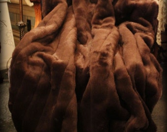 May include: A brown faux fur throw blanket draped over a chair. The blanket is soft and plush, and it has a luxurious feel. The text "Fur Accents Plush Pelt Throws" is printed on the blanket.