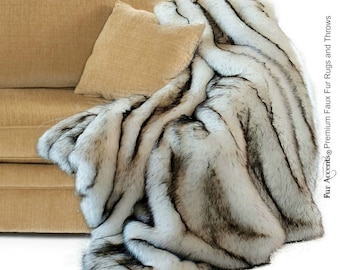 May include: A white and black faux fur throw blanket draped over a tan couch. The blanket has a long, shaggy pile and is made of soft, luxurious faux fur.