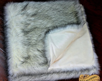 May include: A white faux fur throw blanket with a black tipped fur trim. The blanket is folded in half and has a cream colored fleece lining.