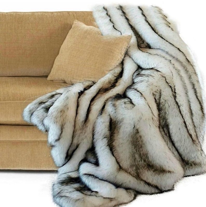 Pu&ograve; includere: Una coperta in pelliccia sintetica bianca e nera con un motivo a righe. La coperta &egrave; drappeggiata su un divano beige.