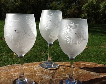 Könnte beinhalten: Drei gefrostete Weingläser aus Glas mit einem in das Glas geätzten Pfauenfeder-Design. Jedes Glas hat einen kleinen Strassstein in der Mitte des Federdesigns.