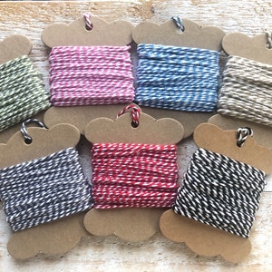 May include: Six spools of baker's twine in various colours, including green, pink, blue, beige, black, and red. Each spool is made of cardboard and has a hole in the centre for hanging.