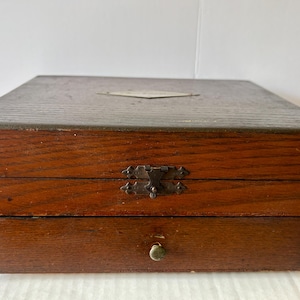 May include: A vintage wooden box with a drawer. The box is made of dark brown wood with a rectangular shape. It has a metal clasp and a small drawer with a round knob. A small diamond-shaped metal plate is on the top.