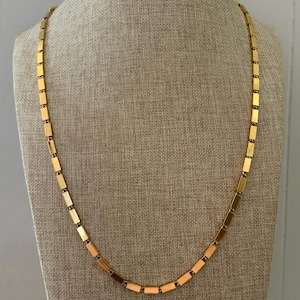 May include: A gold-coloured necklace featuring a rectangular link design. The necklace is displayed on a neutral-toned mannequin, highlighting its length and style. The links are evenly spaced, creating a sleek and modern appearance.
