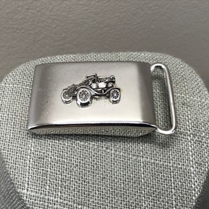 May include: A silver belt buckle with a vintage car design. The car is detailed with wheels, a windshield, and a roof.