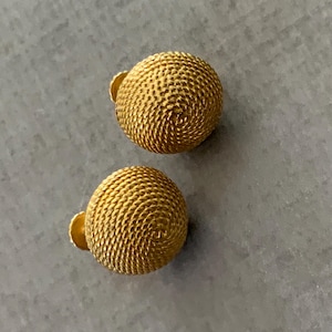 May include: Two gold-colored, textured ball earrings with a post backing. The earrings have a woven or coiled design, and are set against a gray background. The earrings are a classic jewelry item.