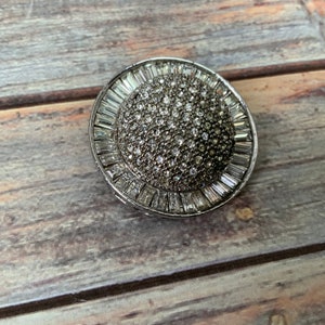 May include: A silver-toned brooch with a round, faceted crystal center surrounded by a ring of baguette-shaped crystals.