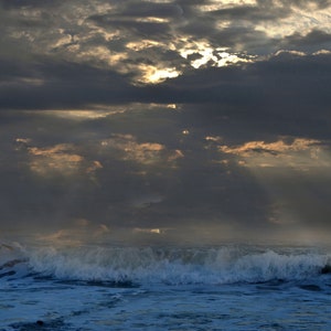 May include: A dramatic seascape with a dark, stormy sky and a single wave crashing in the foreground. The sun is shining through the clouds, creating a ray of light.