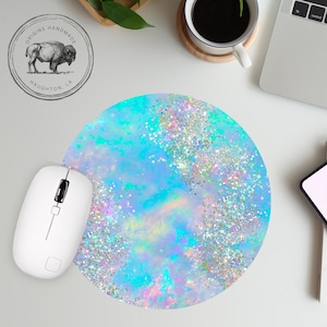 May include: A round blue and turquoise mouse pad with a glittery iridescent design. The mouse pad is on a white surface with a computer mouse and a laptop.