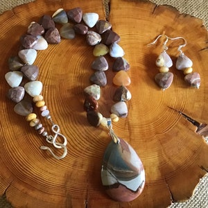 May include: A multi-colored gemstone necklace and matching earrings. The necklace features a large teardrop-shaped pendant and is made with triangular and round beads. The earrings are made with triangular beads.