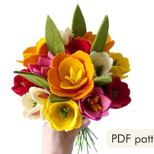 May include: A felt flower bouquet with yellow, orange, pink, red, and white flowers. The bouquet is held in a hand and has green leaves. PDF pattern.
